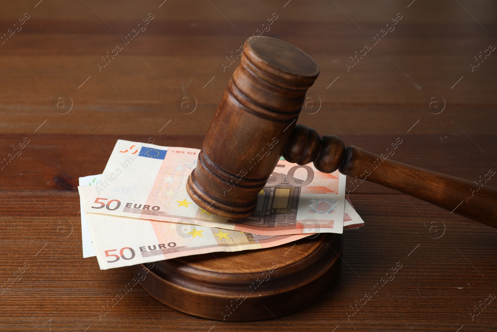 Photo of Alimony. Money between judge's gavel and sound block on wooden table, closeup