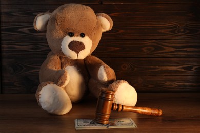 Photo of Alimony. Toy bear, gavel and dollar banknotes on wooden table