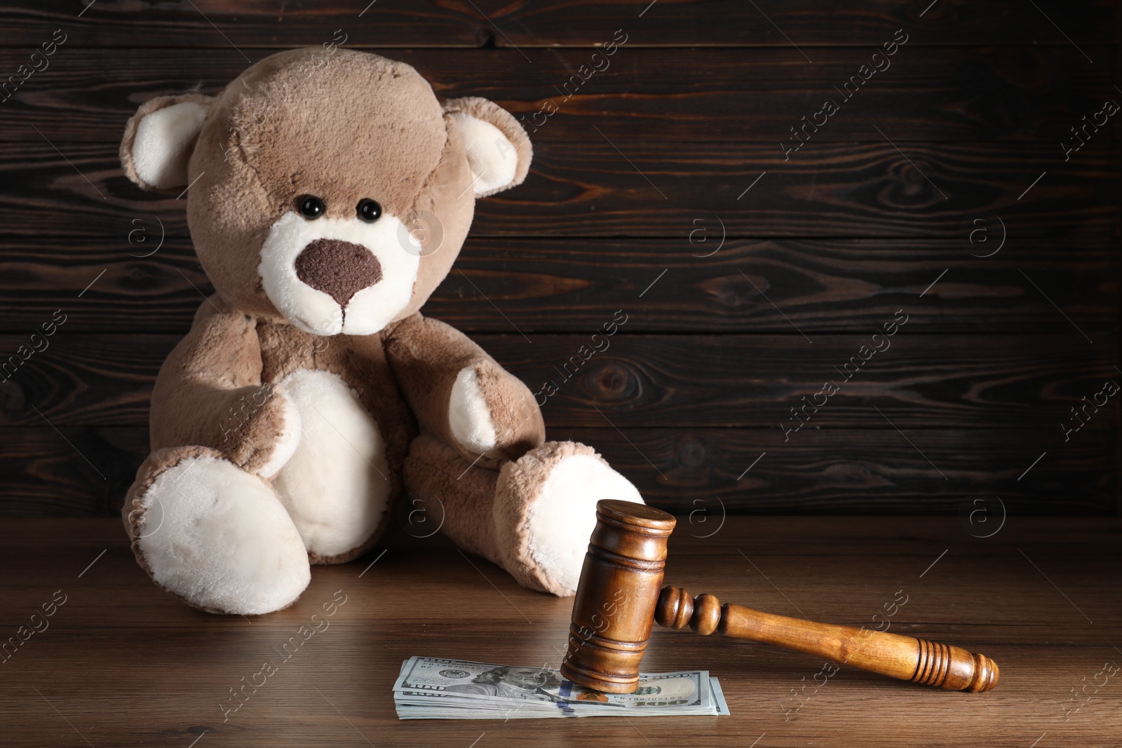 Photo of Alimony. Toy bear, gavel and dollar banknotes on wooden table