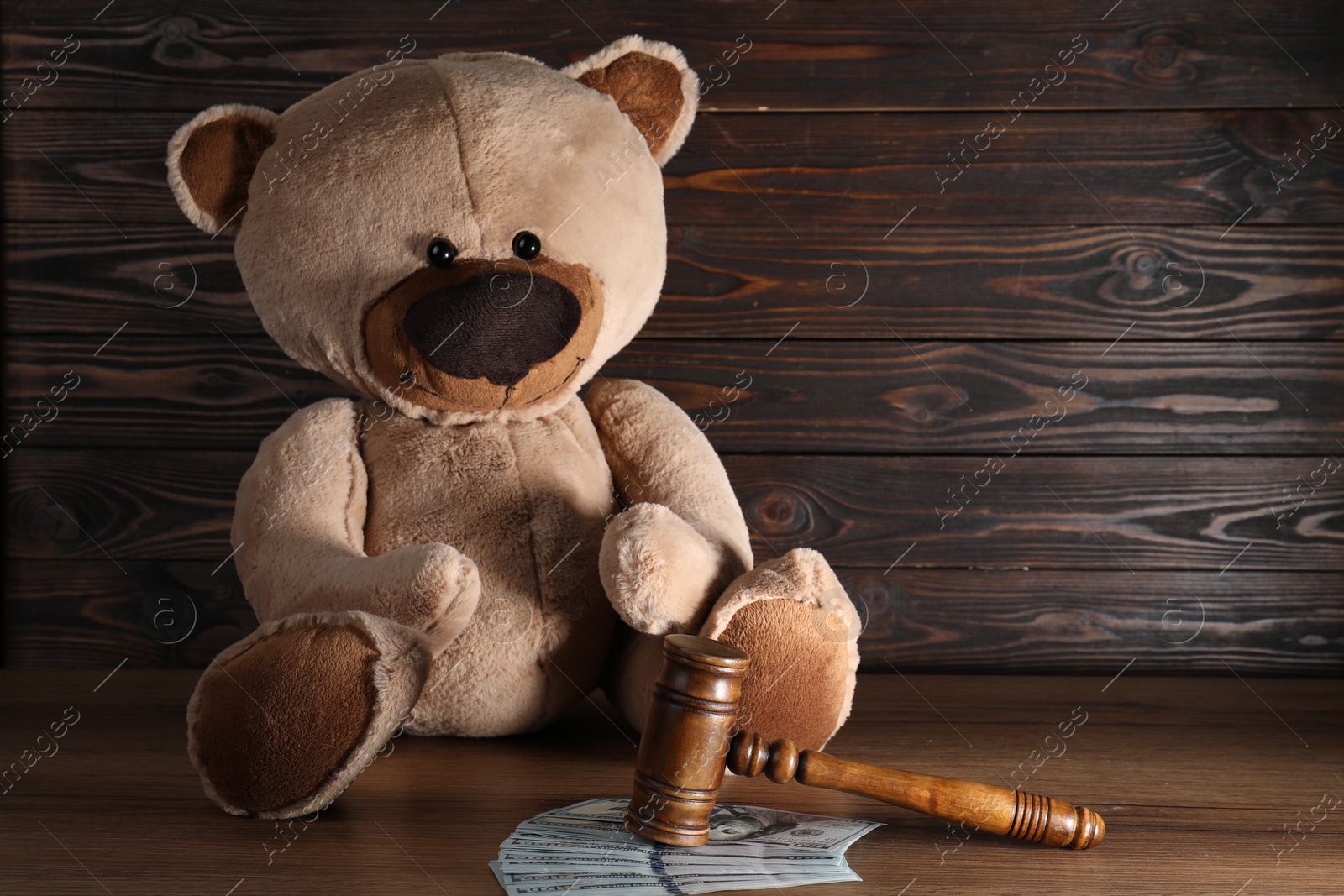 Photo of Alimony. Toy bear, gavel and dollar banknotes on wooden table