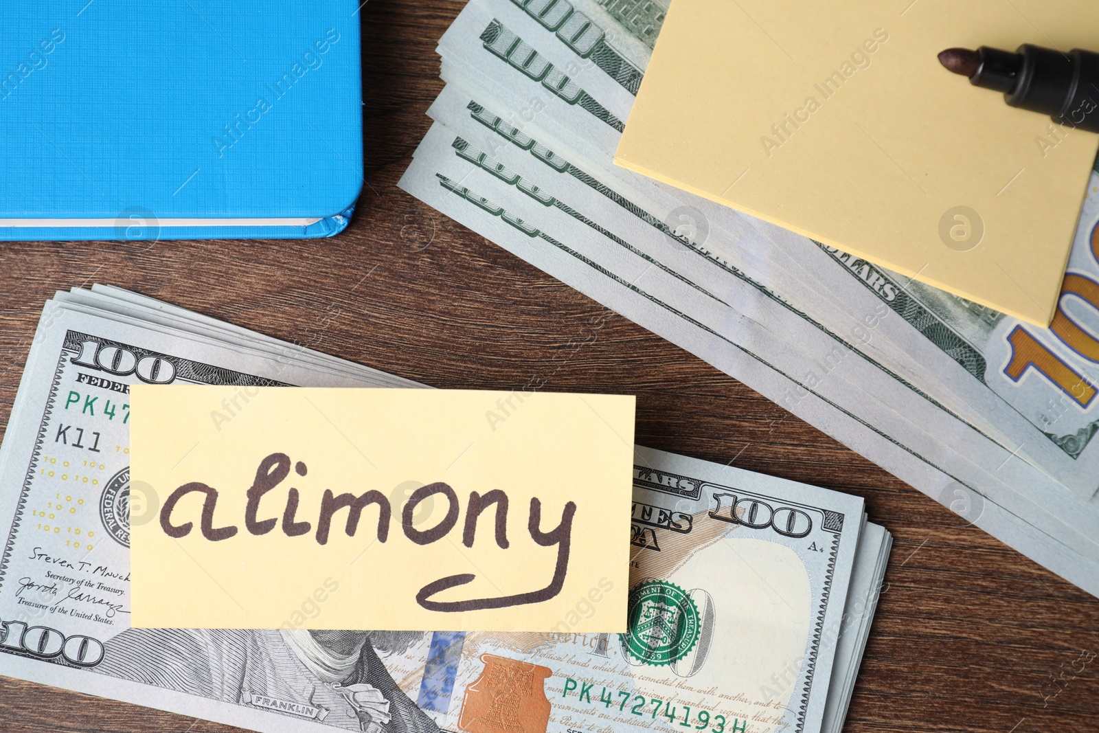 Photo of Card with word Alimony, dollar banknotes, felt pen and notebook on wooden table, top view