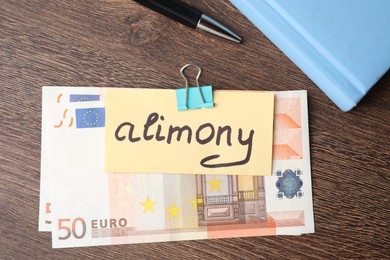 Photo of Card with word Alimony, euro banknotes, notebook and pen on wooden table, top view