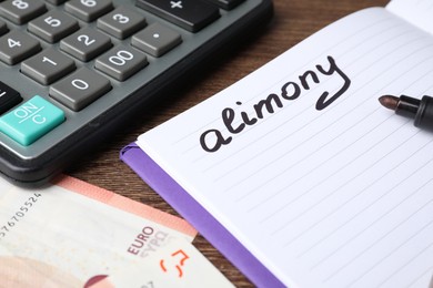 Notebook with word Alimony, euro banknotes, felt pen and calculator on wooden table, closeup