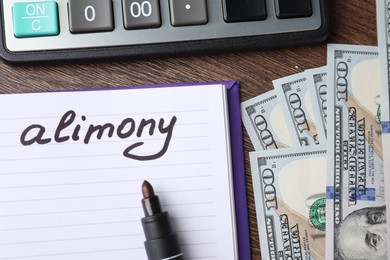 Notebook with word Alimony, dollar banknotes, felt pen and calculator on wooden table, top view