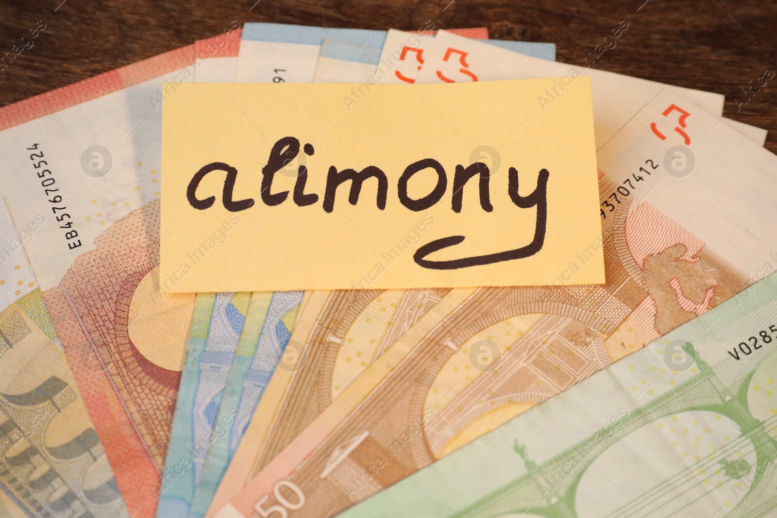 Photo of Card with word Alimony and euro banknotes on wooden table, closeup