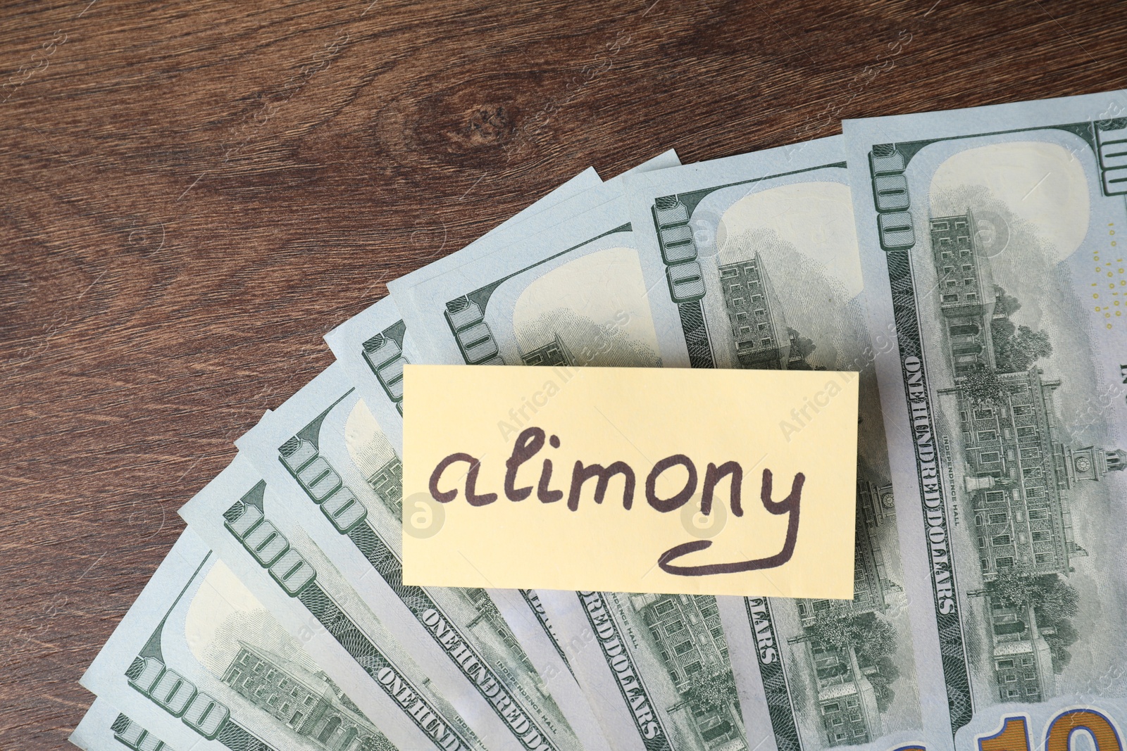 Photo of Card with word Alimony and dollar banknotes on wooden table, top view