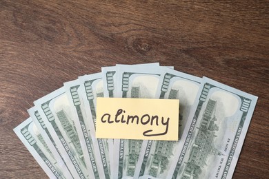 Photo of Card with word Alimony and dollar banknotes on wooden table, top view