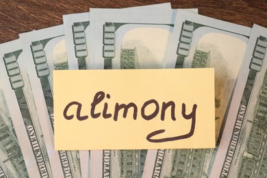 Photo of Card with word Alimony and dollar banknotes on wooden table, top view