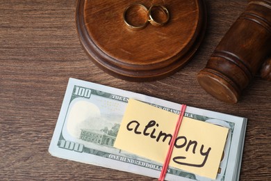 Card with word Alimony, dollar banknotes, gavel and rings on wooden table, above view