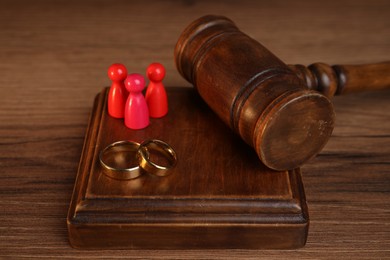 Photo of Alimony. Human figures, gavel and rings on wooden table, closeup