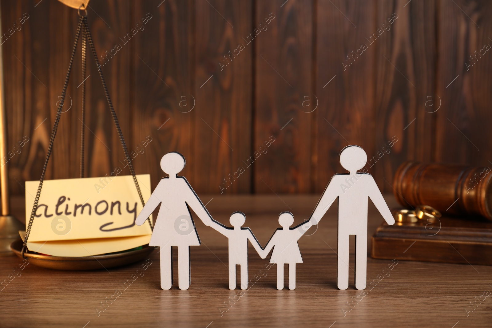 Photo of Card with word Alimony, figures of family, scales, rings and gavel on wooden table