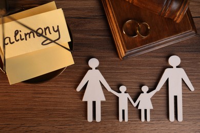 Photo of Card with word Alimony, figures of family, scales, rings and gavel on wooden table, top view