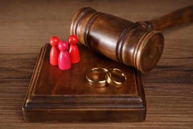 Photo of Alimony. Human figures, gavel and rings on wooden table, closeup