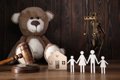 Photo of Alimony. Figures of family, gavel, toy bear, statuette of Lady Justice and house model on wooden table