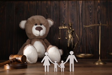 Photo of Alimony. Figures of family, gavel, toy bear, scales and statuette of Lady Justice on wooden table