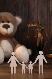 Photo of Alimony. Figures of family, gavel, toy bear, statuette of Lady Justice and scales on wooden table