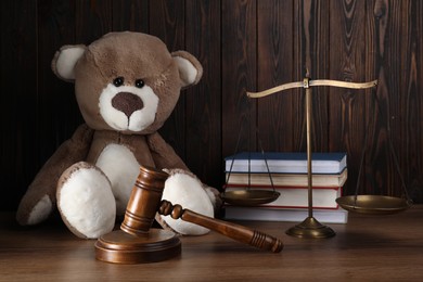 Photo of Alimony. Toy bear, gavel, scales and books on wooden table