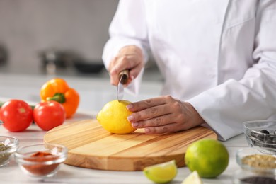 Professional chef cutting lemon at table in kitchen, closeup