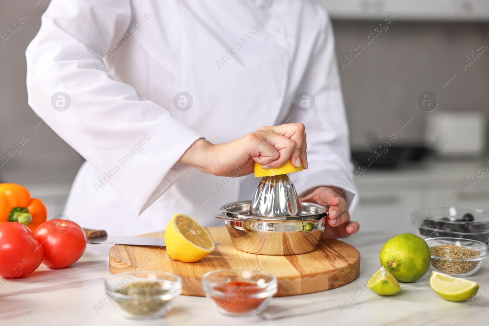 Photo of Woman squeezing juice out of lemon at table in kitchen, closeup