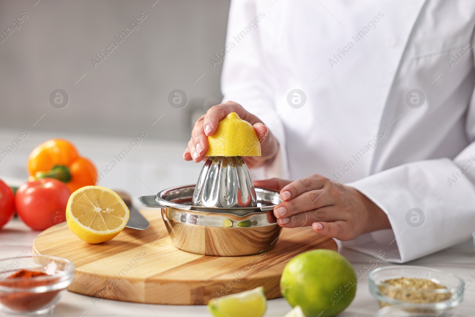 Photo of Woman squeezing juice out of lemon at table in kitchen, closeup