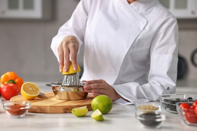 Woman squeezing juice out of lemon at table in kitchen, closeup