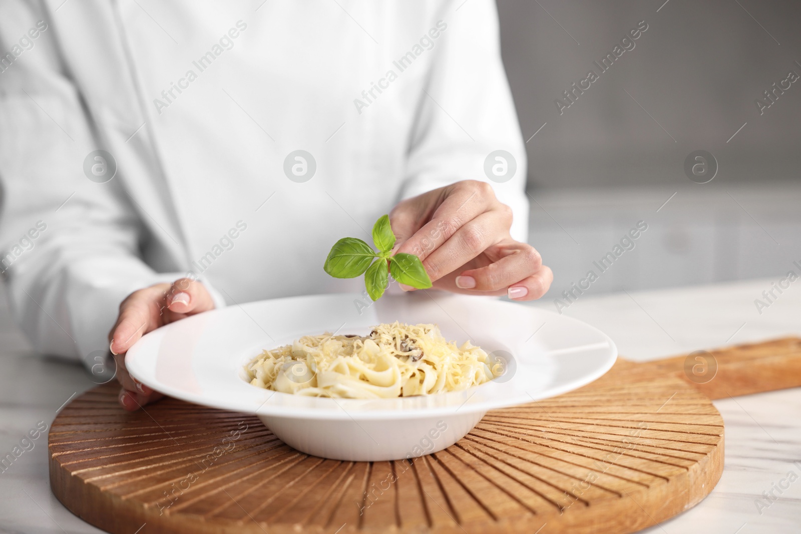 Photo of Professional chef decorating delicious pasta with basil at table in kitchen