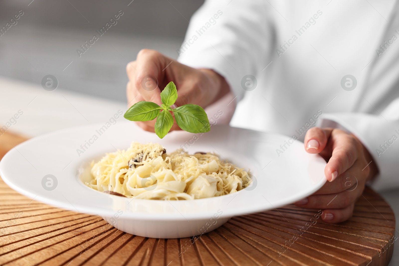 Photo of Professional chef decorating delicious pasta with basil at table in kitchen