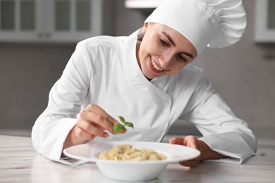 Professional chef decorating delicious pasta with basil at white marble table in kitchen