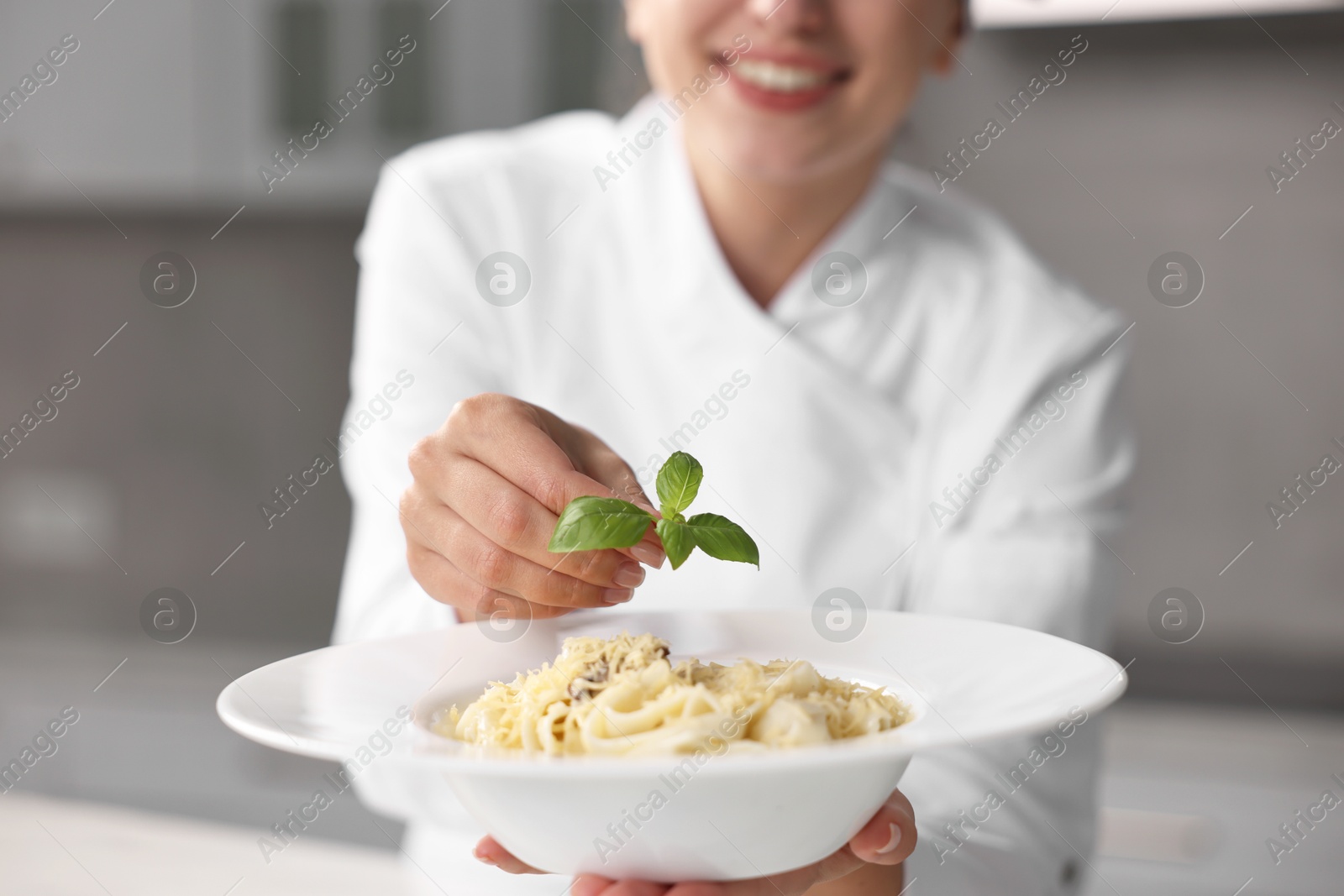 Photo of Professional chef decorating delicious pasta with basil in kitchen