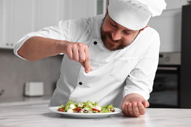 Professional chef adding salt to delicious salad at white marble table in kitchen