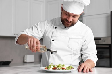 Photo of Professional chef pouring oil onto delicious salad at white marble table in kitchen