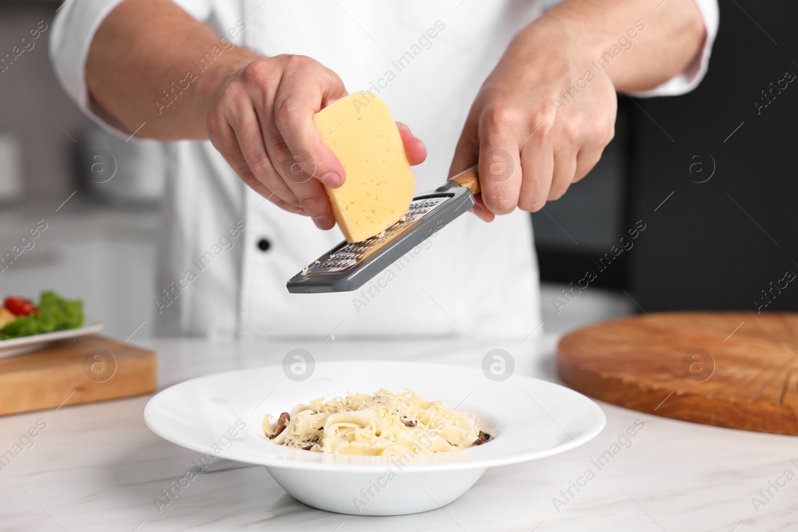 Photo of Professional chef grating cheese into delicious dish at white marble table in kitchen, closeup