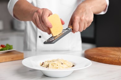 Photo of Professional chef grating cheese into delicious dish at white marble table in kitchen, closeup