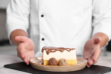 Professional chef with delicious cake at table in kitchen, closeup