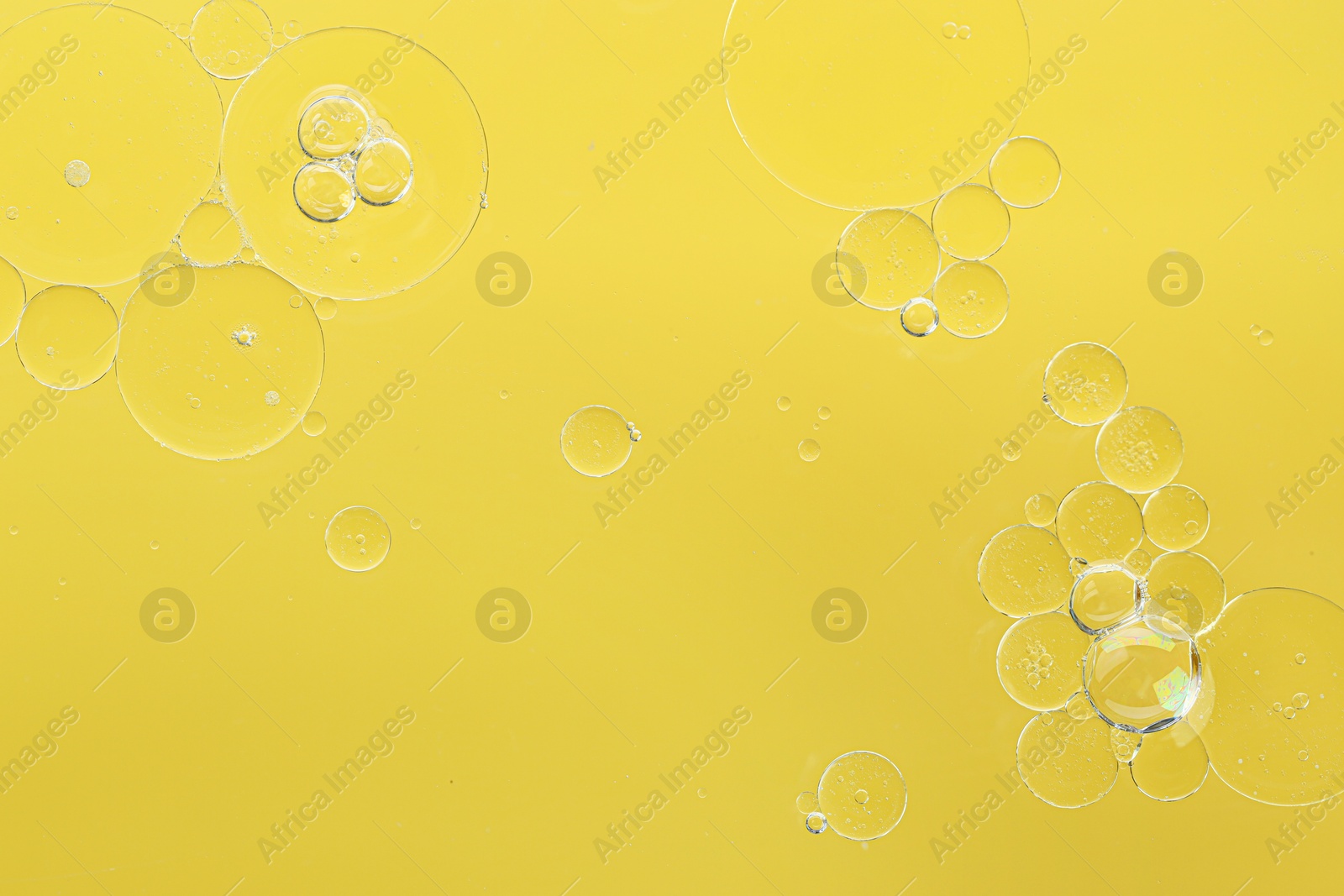 Photo of Essential oil bubbles on yellow background, macro view. Cosmetic product