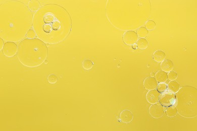 Photo of Essential oil bubbles on yellow background, macro view. Cosmetic product