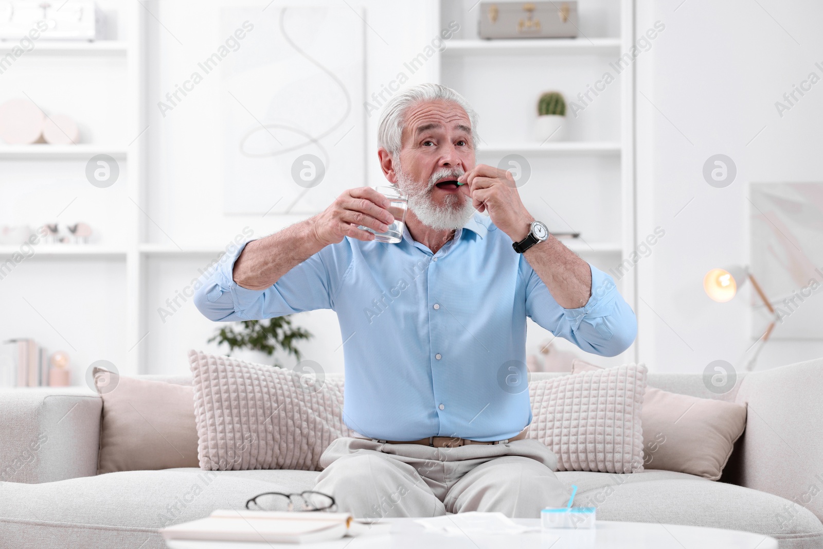 Photo of Senior man with glass of water taking pill at home