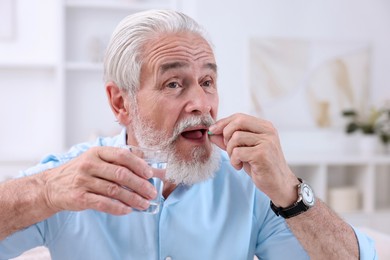 Senior man with glass of water taking pill at home