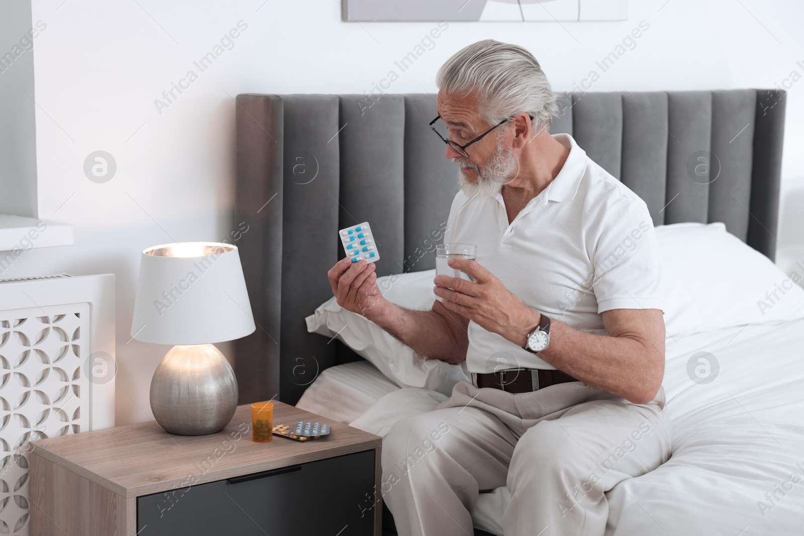 Photo of Senior man with glass of water and pills on bed at home