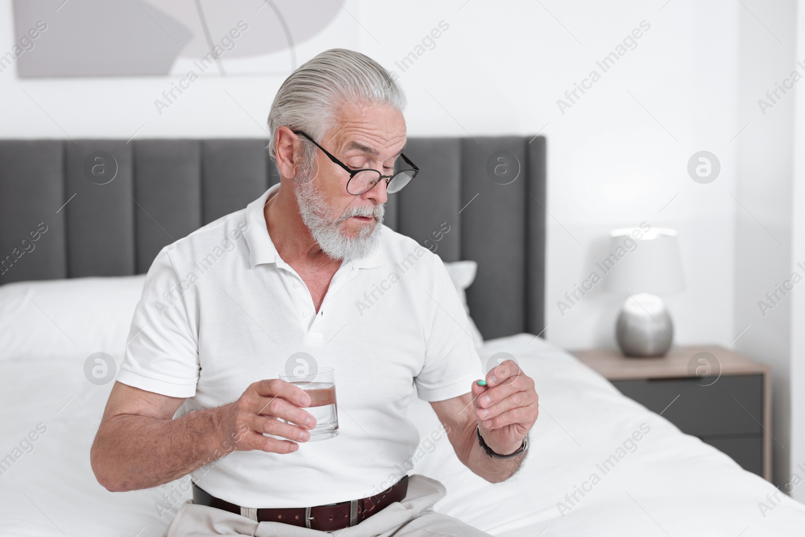 Photo of Senior man with glass of water and pill on bed at home