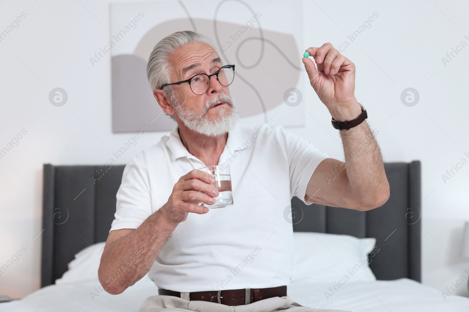 Photo of Senior man with glass of water and pill on bed at home