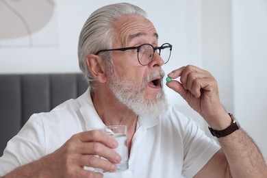 Senior man with glass of water taking pill at home