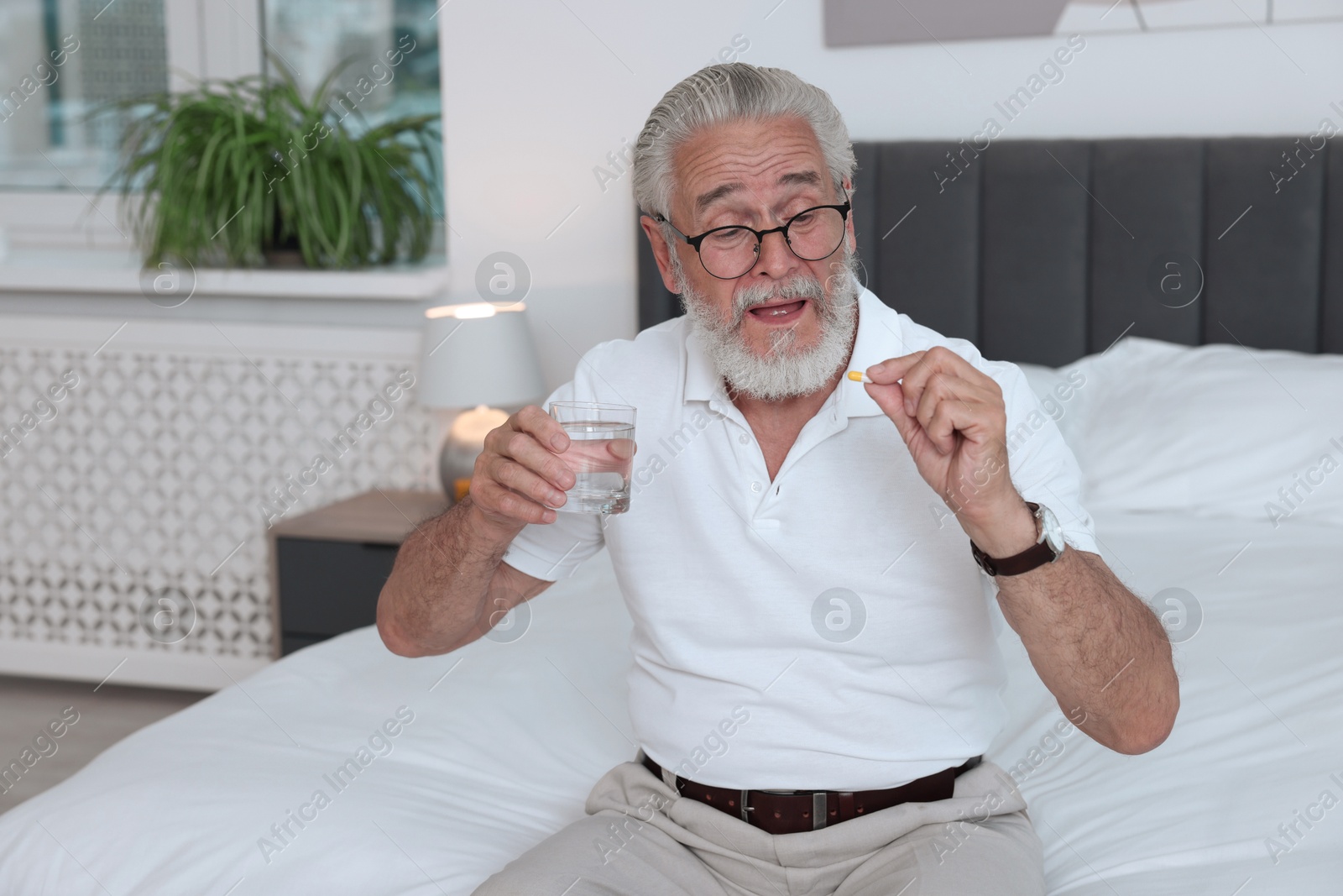 Photo of Senior man with glass of water and pill on bed at home