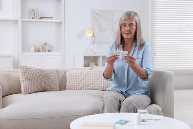 Senior woman holding blister with pills at home