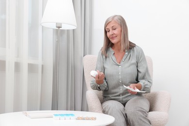 Photo of Senior woman with bottle of pills and medicine instruction in armchair at home