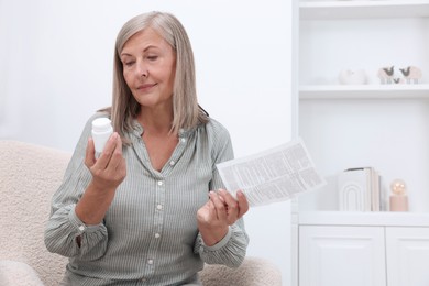 Photo of Senior woman with bottle of pills and medicine instruction in armchair at home