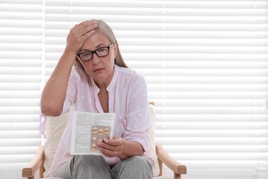 Photo of Senior woman with pills reading medicine instruction in armchair at home, space for text