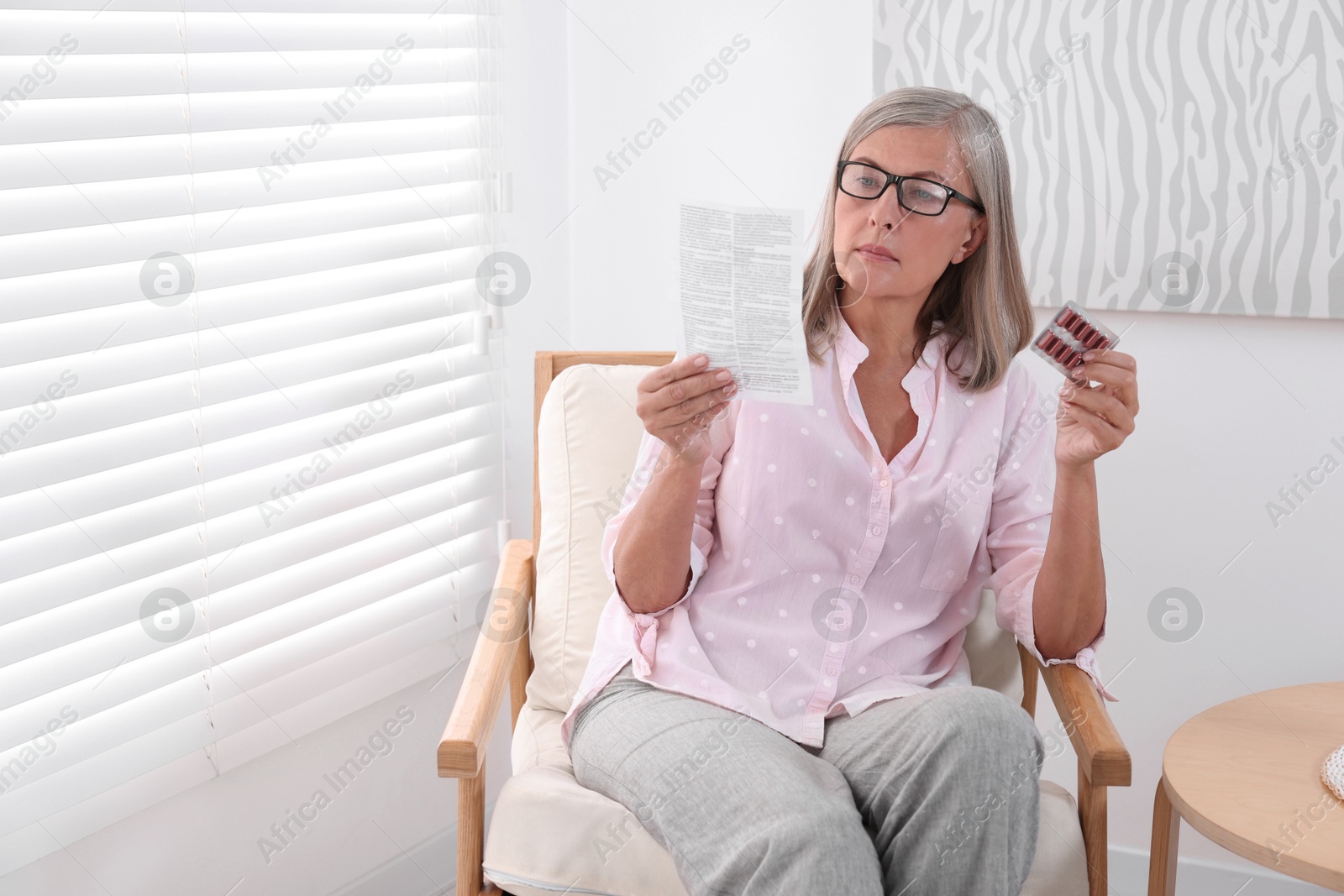 Photo of Senior woman with pills reading medicine instruction in armchair at home, space for text