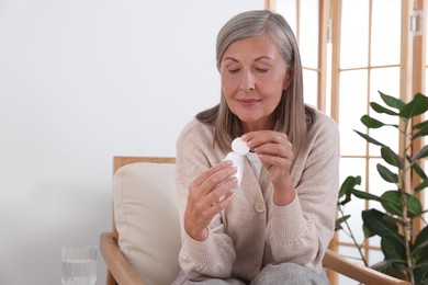 Photo of Senior woman with bottle of pills in armchair at home