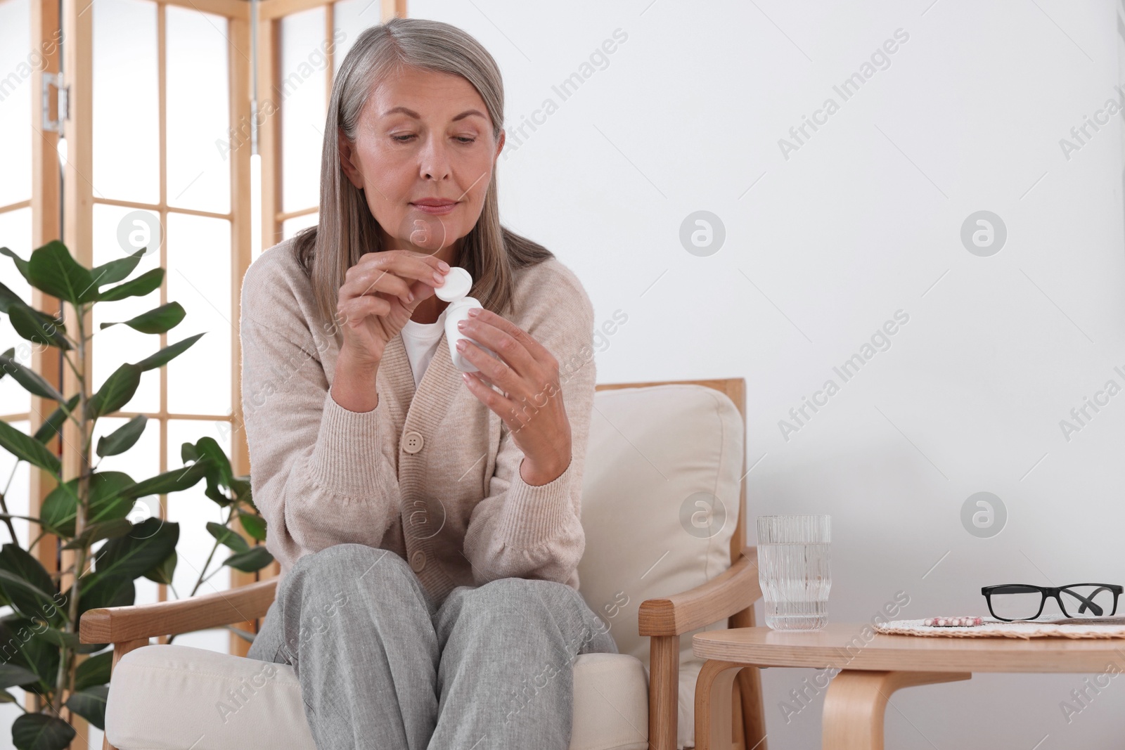 Photo of Senior woman with bottle of pills in armchair at home